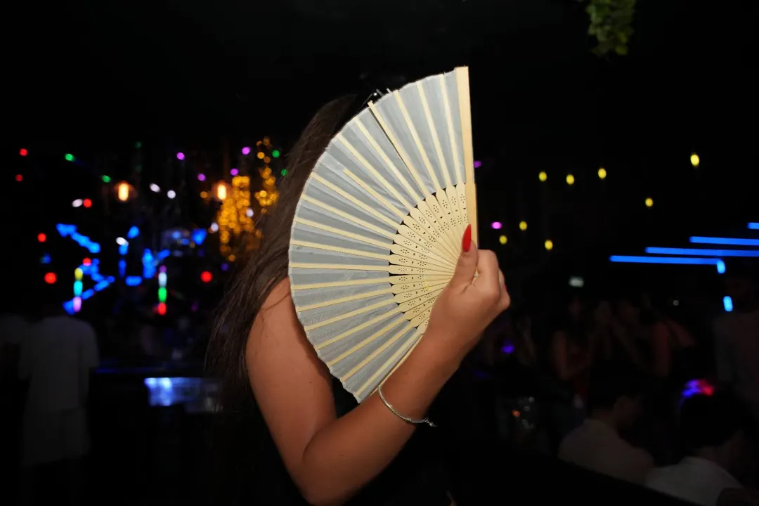 צעירה עם מניפה במסיבת נוער חוץ עם אורות צבעוניים